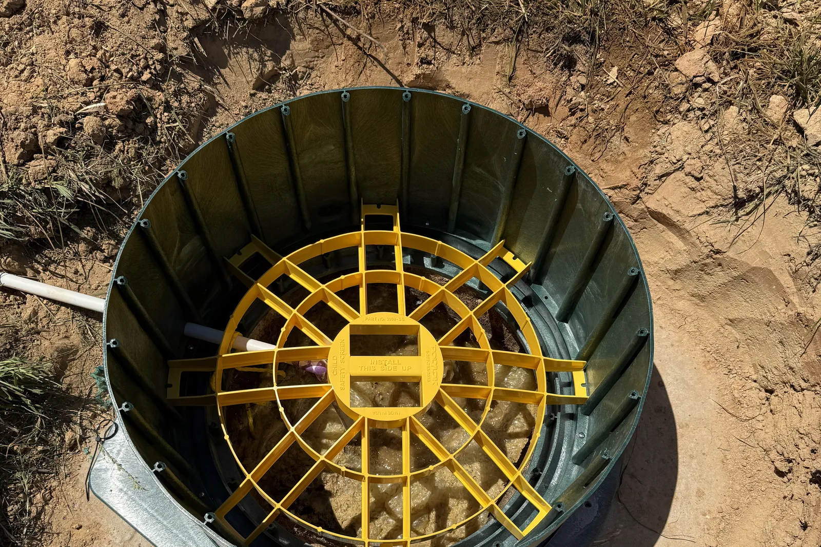 Yellow safety screen fitted across the septic tank opening inside the riser