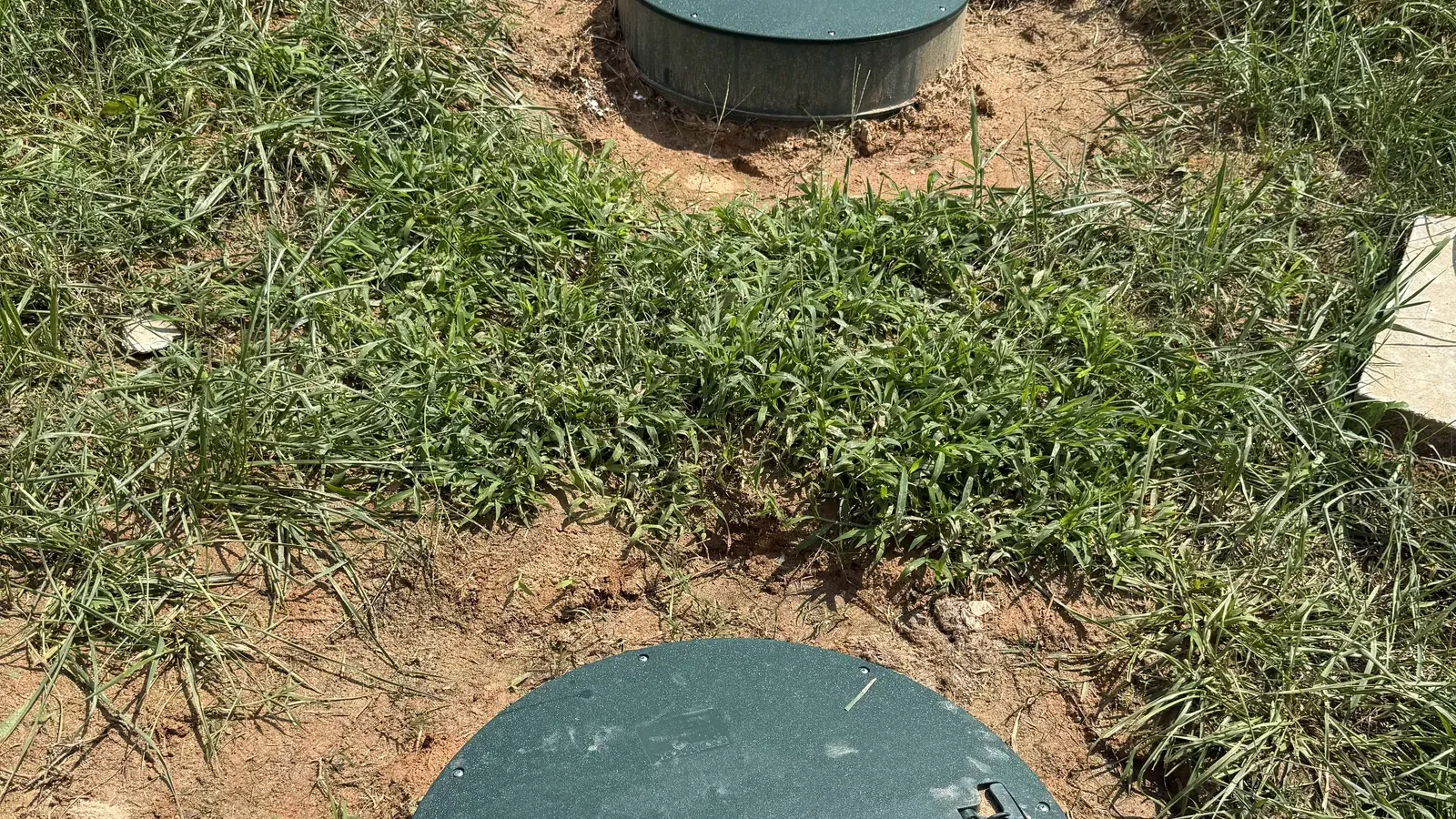 Two septic riser lids set at ground level in red clay soil, the tank access Septic Samurai adds during septic system repair in Lexington, NC